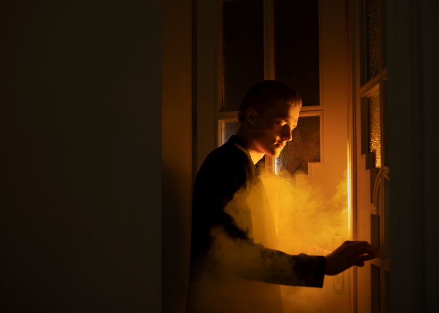 Afbeelding: Mysterieuze foto van een man bij een deur met warm tegenlicht en rook voor storytelling in fotografie