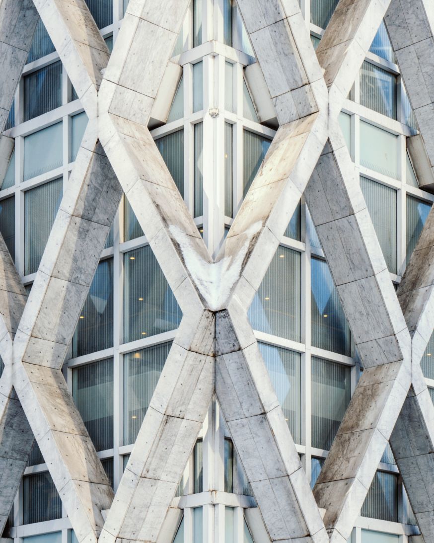 Afbeelding: Detail van een moderne gevel met herhalende kruisvormen, betonnen structuur en strakke ramen in een grafisch patroon
