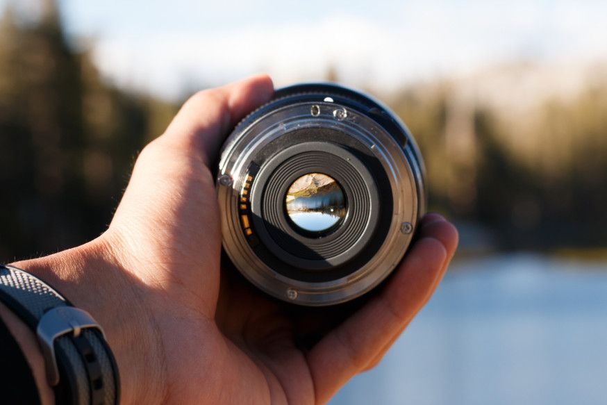 Afbeelding: Een hand houdt een cameralens vast waar een landschap doorheen te zien is