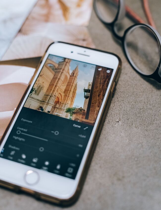 Afbeelding: Smartphone met een architectuurfoto in een bewerkingsapp, naast een bril op tafel
